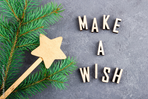 Text MAKE A WISH made from wooden letters. Christmas tree branch with magic wand with a star. Xmas and New Year's concept.