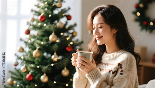 Woman wearing a cozy sweater holding a mug near the Christmas tree soft natural light