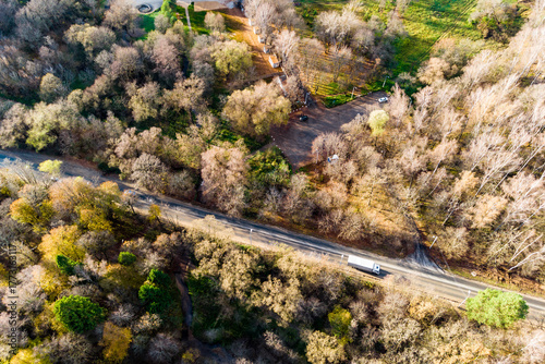 Photography Aerial shot of a white truck cruising down a rural road through a colorful autumn forest
