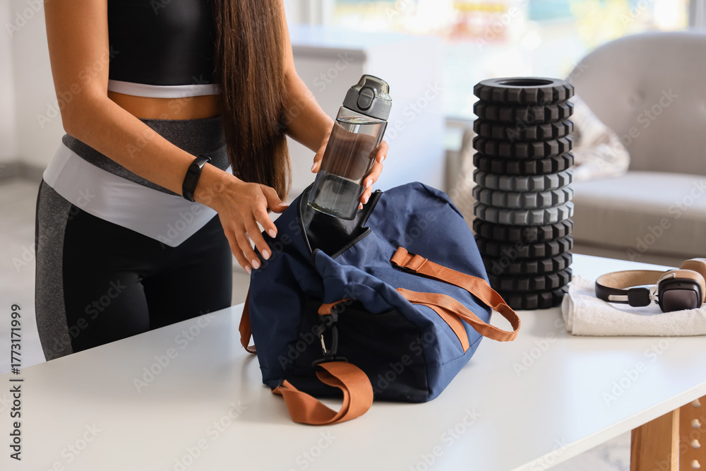 Φωτογραφία Sporty young woman putting bottle of water in bag at home, closeup