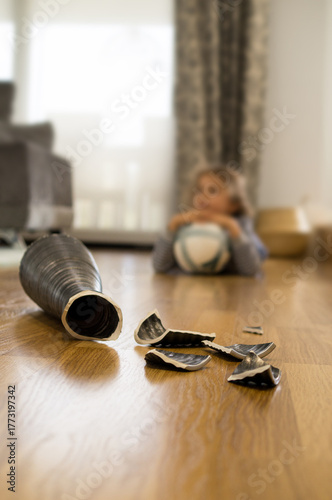 Fotografie A child, out of focus, in the living room, staring at the vase he just broke with a ball