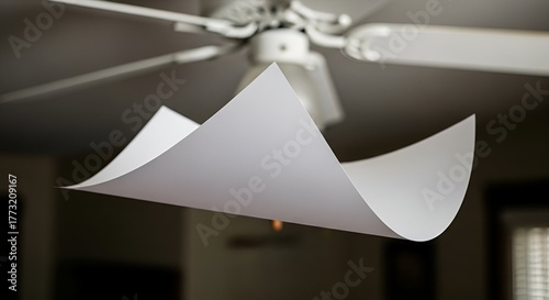 White paper sheet bending in mid-air with a ceiling fan in the blurry background