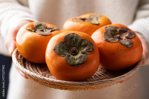 Ripe persimmon fruit in basket holding by hand, Autumn fruit
