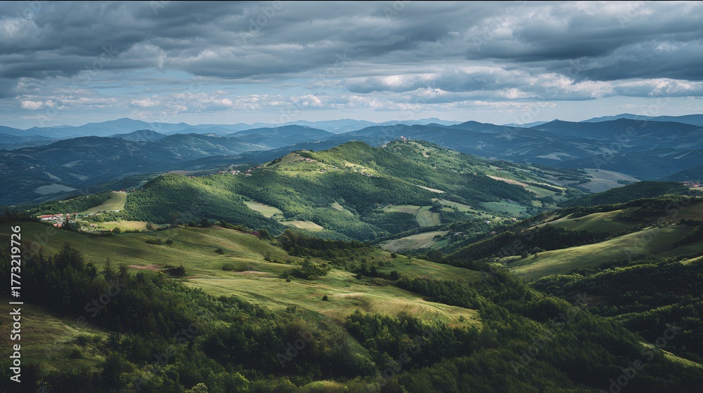 Fototapeta premium Rolling green hills and verdant valleys stretch beneath a dramatic, overcast sky.