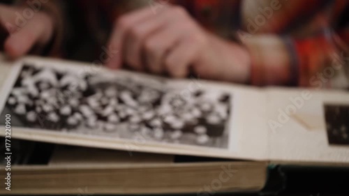 man looks at an old photo album and remembers past. flips through pages in blur black and white photographs. concept of nostalgia and memories youth. close-up. front view.