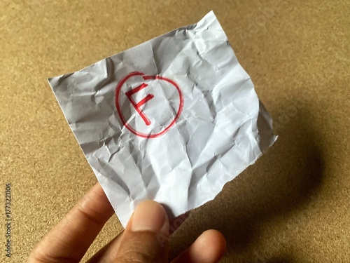 A person is holding a small, crumpled piece of paper with the failing grade 