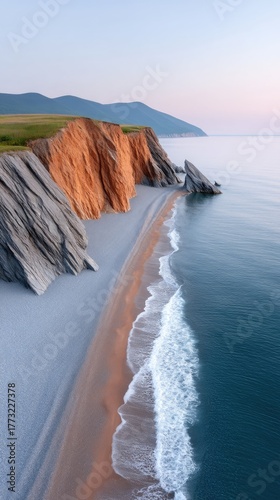 Rugged Coastal Cliffs Meet Gentle Ocean Waves During Golden Hour with Sandy Beach and Distant Haze Over Water in a Serene Natural Landscape
