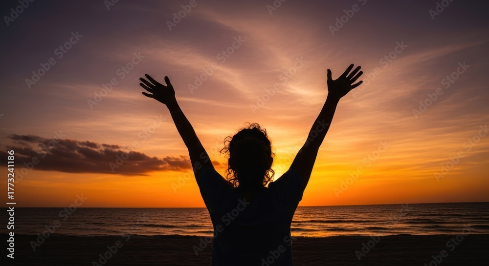 Fototapeta premium A woman with arms raised against a vibrant sunset sky.