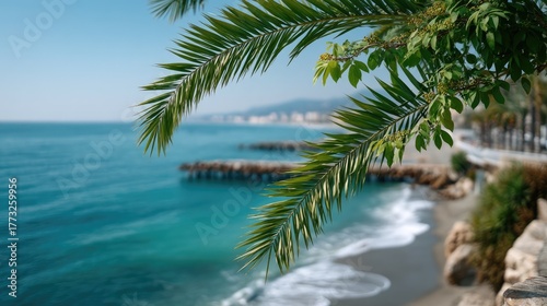 Vibrant Green Palm Fronds Frame a Serene Beach Scene with Turquoise Ocean and Distant Coastal Town Under Clear Blue Sky