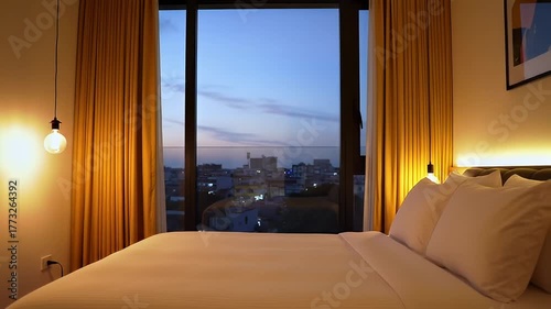 Luxury Hotel Room with Ocean View at Dusk Featuring Golden Curtains and Modern Lighting and Cityscape Outside the Window with Soft Ambient Light Filling the Space
