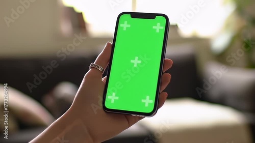 Close Up Of A Hand Holding A Smartphone With A Green Screen Display In A Well Lit Living Room With A Blurry Background