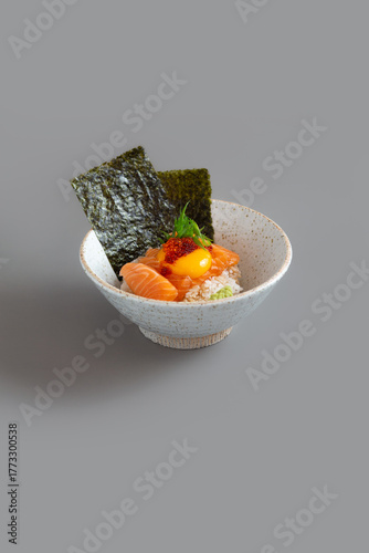 Salmon Donburi Japanese food style with egg yolk and Nori on grey background.