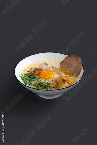 Ramen noodle in broth with Chashu pork, fresh green onions and egg yolk in bowl.