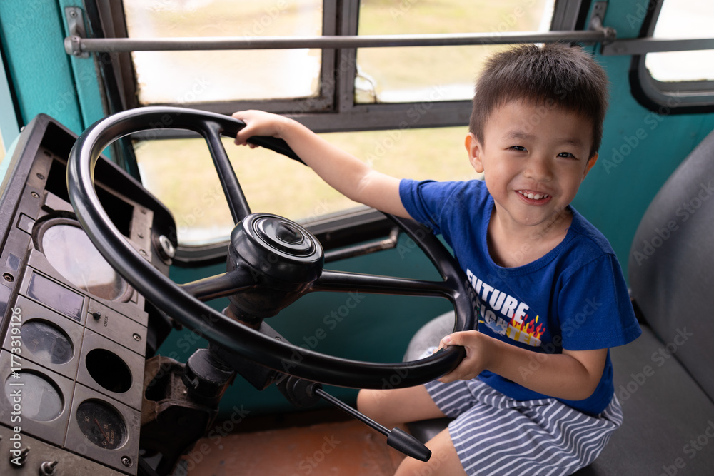Obraz premium Happy asian boy pretending to be a bus driver, holding steering wheel and smiling