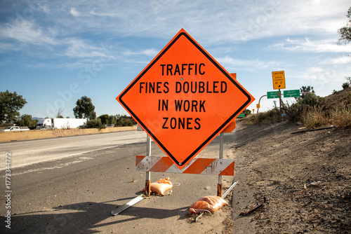 Orange traffic sign stating Traffic Fines Doubled in Work Zones with traffic in the background