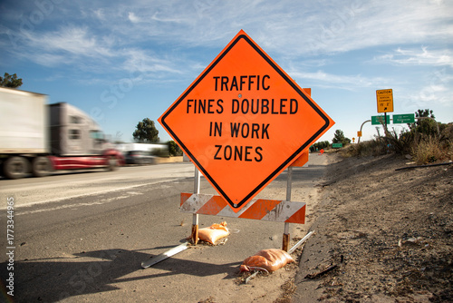 Orange traffic sign stating Traffic Fines Doubled in Work Zones with traffic in the background