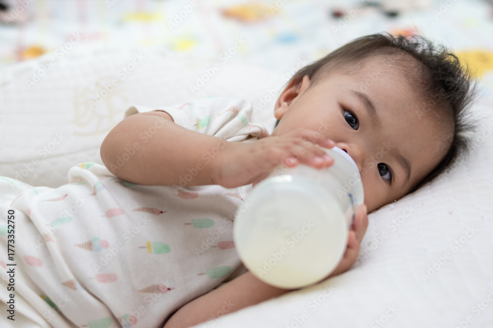 Fototapeta premium Adorable baby girl drinking milk from bottle lying on bed