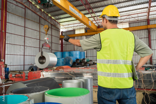 Foto A Safety worker giving instructions and directing the movement of a large metal coil roll being lifted by an overhead crane in a factory
