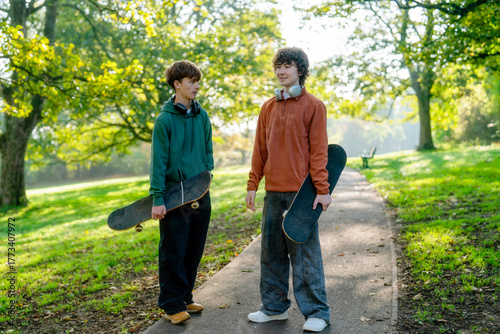 Fotografija Two teens enjoy a sunny morning skateboarding in a peaceful park surrounded by g