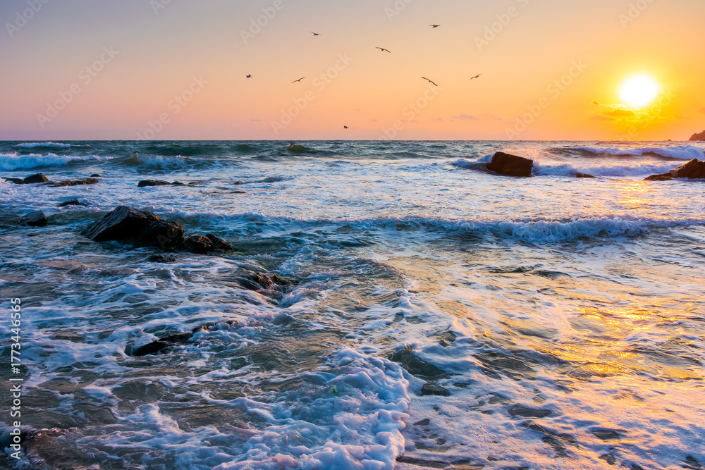 Naklejka premium beautiful sunrise at the sea beach. sandy coast with rock. summer vacation background. sun over horizon. calm waves under orange sky in morning light. amazing seascape for best memories from bulgaria