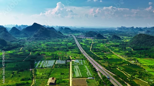 Aerial view of a modern highway passing through lush green farmland and karst mountain scenery in Guilin.