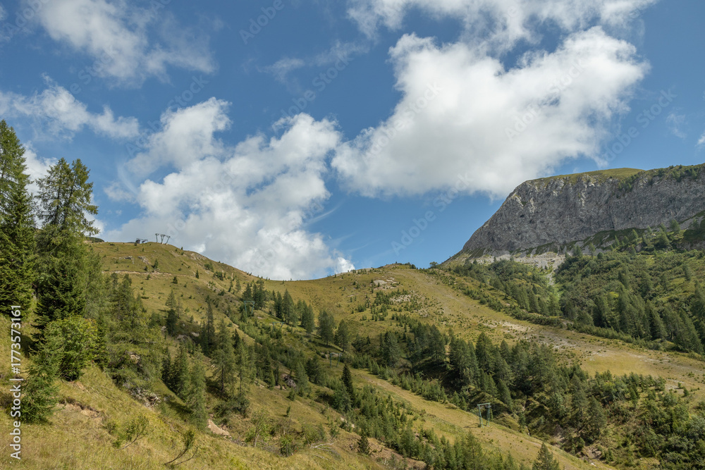Fototapeta premium pendii e cime erbose e rocciose, sotto un cielo azzurro e parzialmente nuvoloso, tra le montagne del nord Italia, in autunno