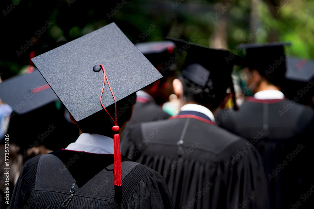 Obraz premium A group of people wearing graduation caps and gowns. The person in the center is wearing a black cap with a red tassel