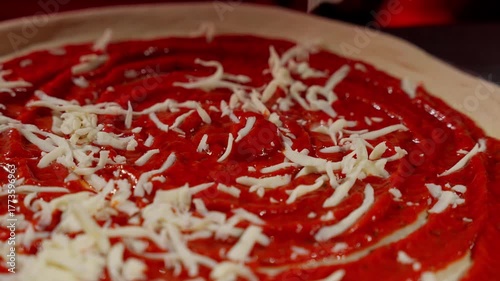 Close-up of pizza dough with tomato sauce and shredded cheese, Unbaked pizza base swirled with red sauce and sprinkled with mozzarella
