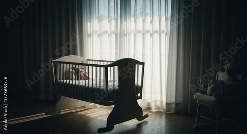 Empty baby crib stands near window with sheer curtains in dark room