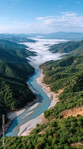 Serene Blue River Meanders Through Lush Green Mountains Under a Sky Filled With Wispy Clouds and Low Fog Rolling Through the Valley