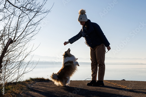 Woman training dog on lakeside path in sunny winter morning