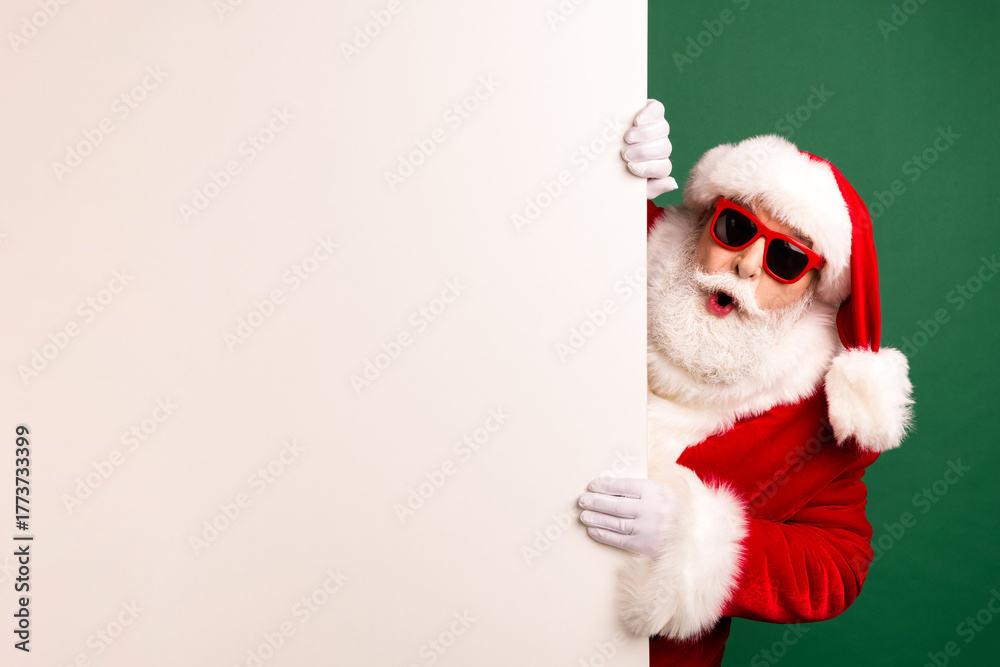 Naklejka premium Santa peeks from a white panel wearing a red suit a hat and sunglass against a green backdrop in a playful holiday scene