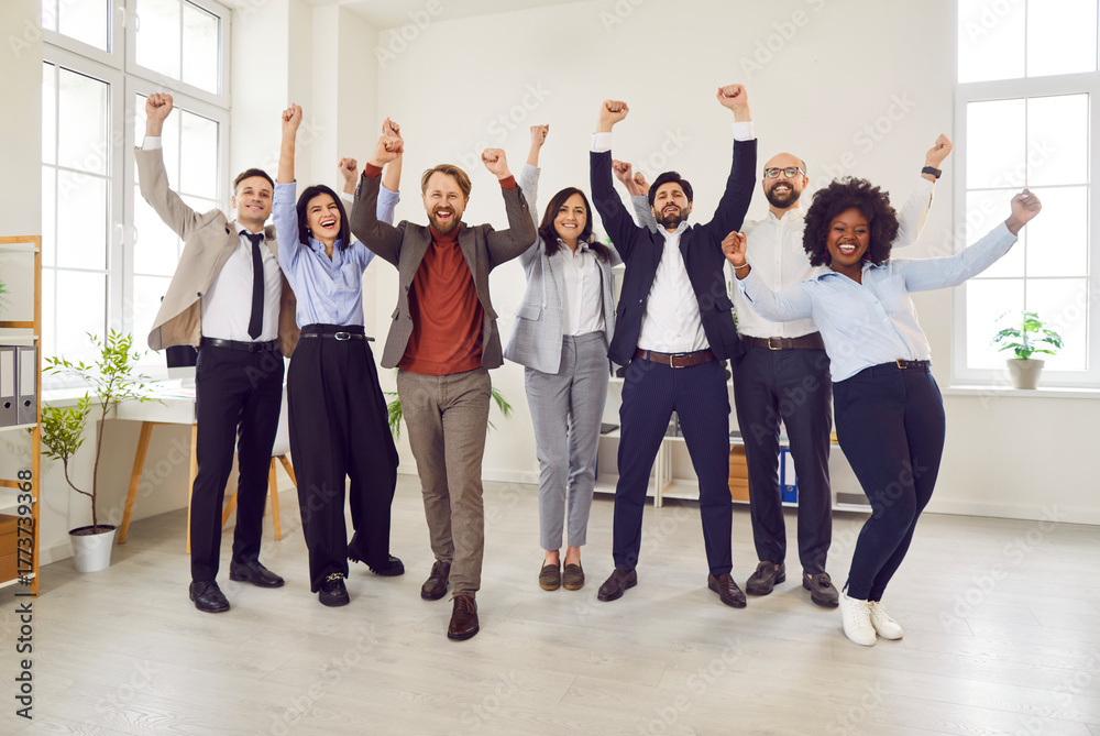Obraz premium Joyful multicultural group of business people at workplace raise their hands up together. Company employees participate in team building. Concept employee engagement, building activity