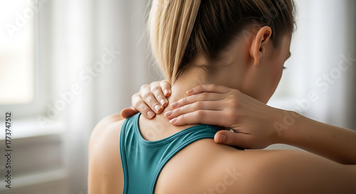 Rear view of an athletic woman massaging her aching neck and tense shoulders, feeling muscle pain from overwork or injury