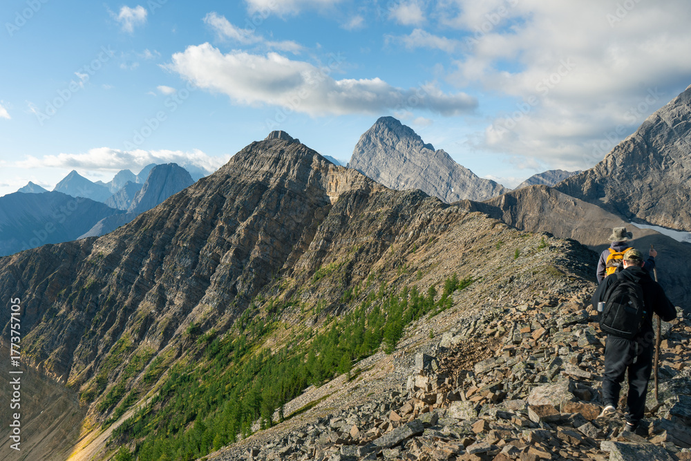Fototapeta premium Hikers traverse a rocky mountain ridge, surrounded by stunning mountain views.