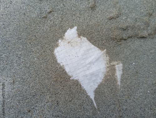 Abstract textured background of rough concrete surface with torn white paper showing woven pattern underneath, conveying decay or discovery