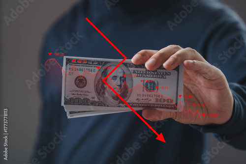 Hand holding US dollar bills with red downward graph overlay, symbolizing financial loss, economic crisis, currency depreciation, investment risk, and stock market downturn.