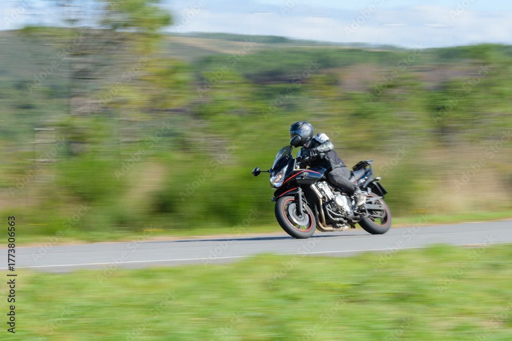 Obraz premium biker on a sport motorcycle rides fast while leaning on a turn on a winding road, motion blur highlighting the dynamic action