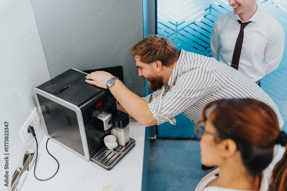 Obraz premium A team of multicultural colleagues maneuvering a compact coffee machine in a sleek office kitchenette, showcasing collaboration and a relaxed, professional atmosphere.