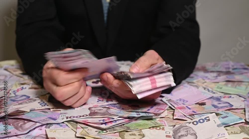 Businessman counts stack of banknotes at desk. Concept of finance, profit, and successful income management. Hands of man sorting paper Ukrainian hryvnia. currency of Ukraine. table is littered money.