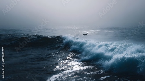 A solitary dolphin or surfer navigates the vast foggy ocean with powerful waves breaking in the foreground under a moody atmosphere