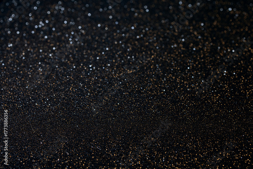 Macro black textured surface with golden glitter in sharp focus at bottom, sparkling grains create cosmic starry illusion blending into soft blur above