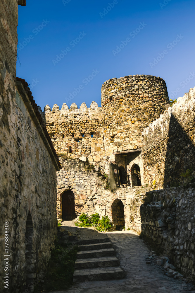 Fototapeta premium Interior courtyard of Ananuri fortress with medieval stone walls, arched doors and a round defensive tower under clear blue sky