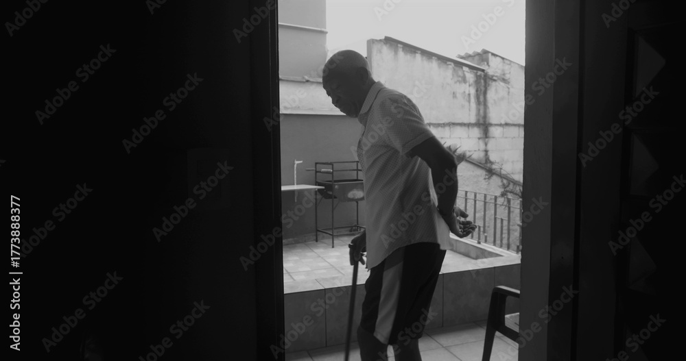Fototapeta premium Elderly man stepping into the porch with a cane, silhouetted in black and white, symbolizing resilience, independence, and reflection in a serene outdoor moment