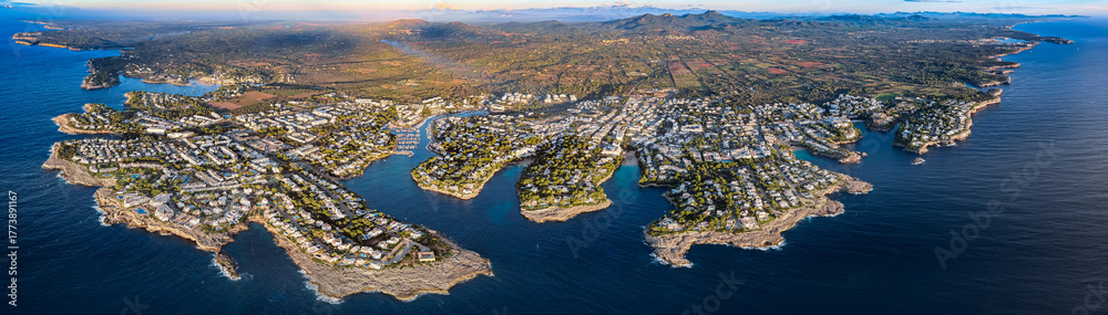 Fototapeta premium Aerial Sunrise Over Cala d'Or: Multiple Coves, Yachts, and Resort Town on Mallorca's Coast