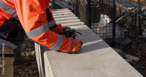 Worker in high-visibility gear writes identification and measurements on a structural concrete column at a construction site. 