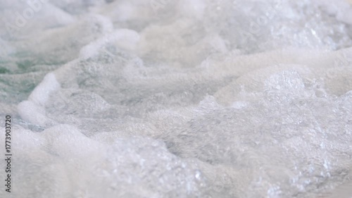 Slow motion view of bubbling water and foam in a jacuzzi, showing dynamic movement, texture, and energy. Air jets create a relaxing, invigorating spa effect with swirling bubbles.