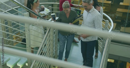 Walking colleagues carrying coffee cups down atrium staircase, with rails and glass panels
