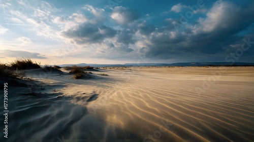 Fototapeta Naklejka Na Ścianę i Meble -  A vast sandy landscape with wind swept dunes rippling sand textures and dramatic clouds at sunset