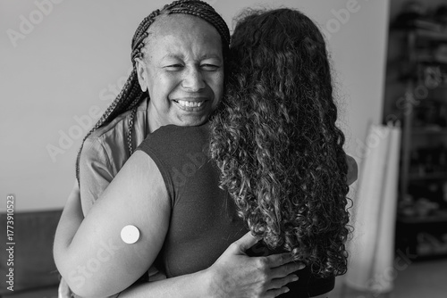 Happy african mother hugging daugher with diabetes patch at home - Family love, lifestyle and disease concept - Black and white editing